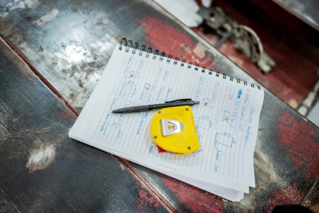 Close-up of notepad with sketches, pen, and tape measure on workbench