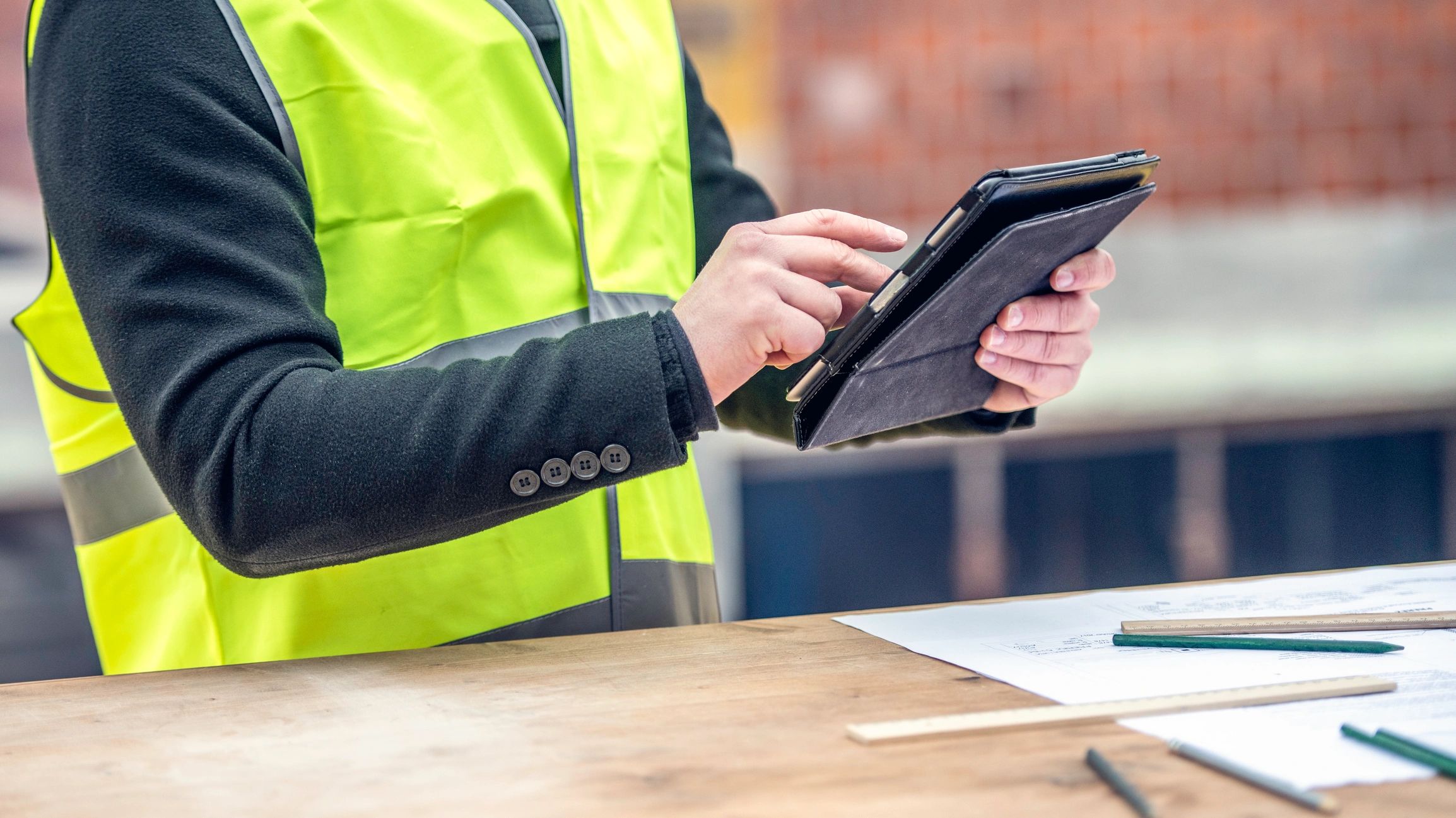 Engineer reviewing construction plans on site with tablet and blueprint